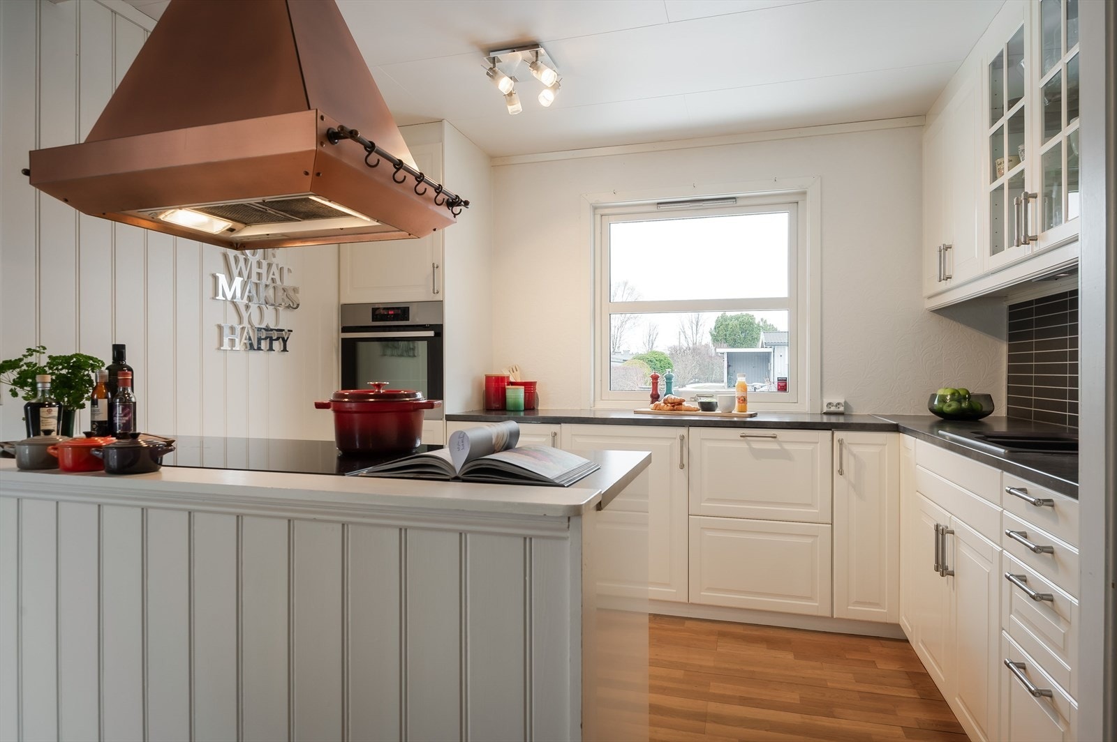 Lyst og pent Ikea-kjøkken med en halvøy mot spisestue som sørger for god skap- og benkeplass. Kjøkkenet er utstyrt med medfølgende integrerte hvitevarer som 80cm bred induksjonstopp, stekeovn i høyskap, oppvaskmaskin og lite kjøleskap. Galleribilde