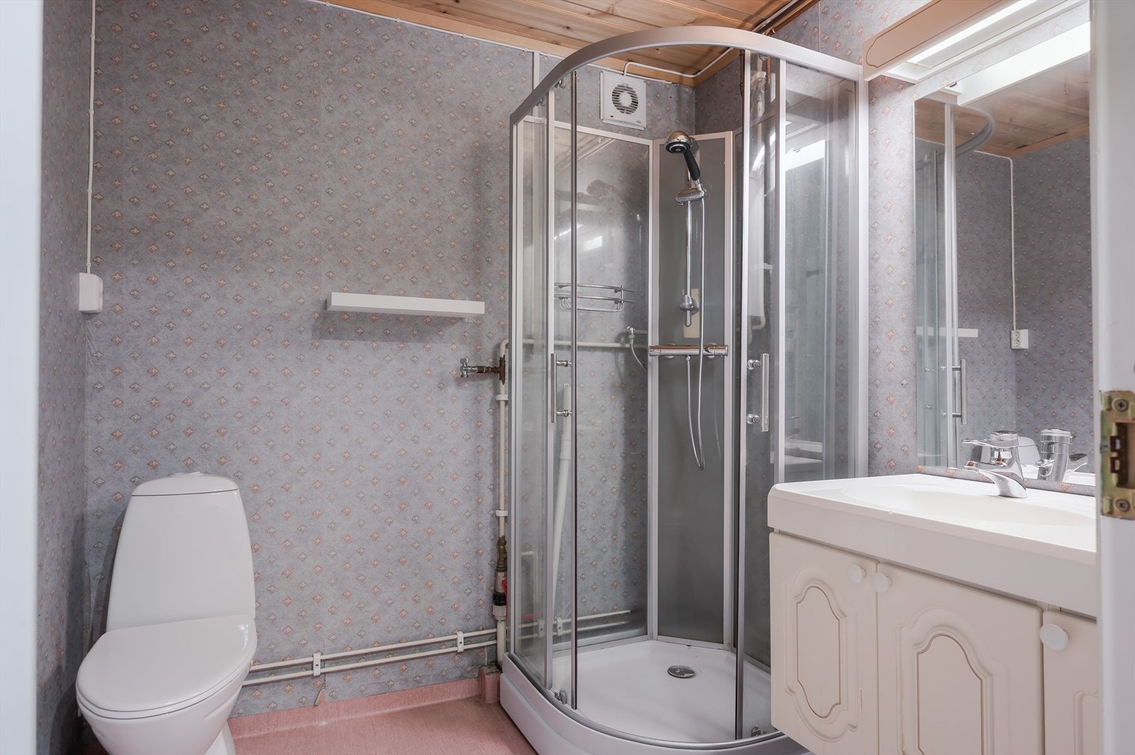 Bad/vaskerom i kjeller med vinylbelegg på gulv med gulvvarme, våtromstapet/belegg på veggene og mekanisk avtrekk. Baderommet er utstyrt med baderomsinnredning med servant, dusjkabinett, gulvstående toalett og opplegg for vaskemaskin. Galleribilde