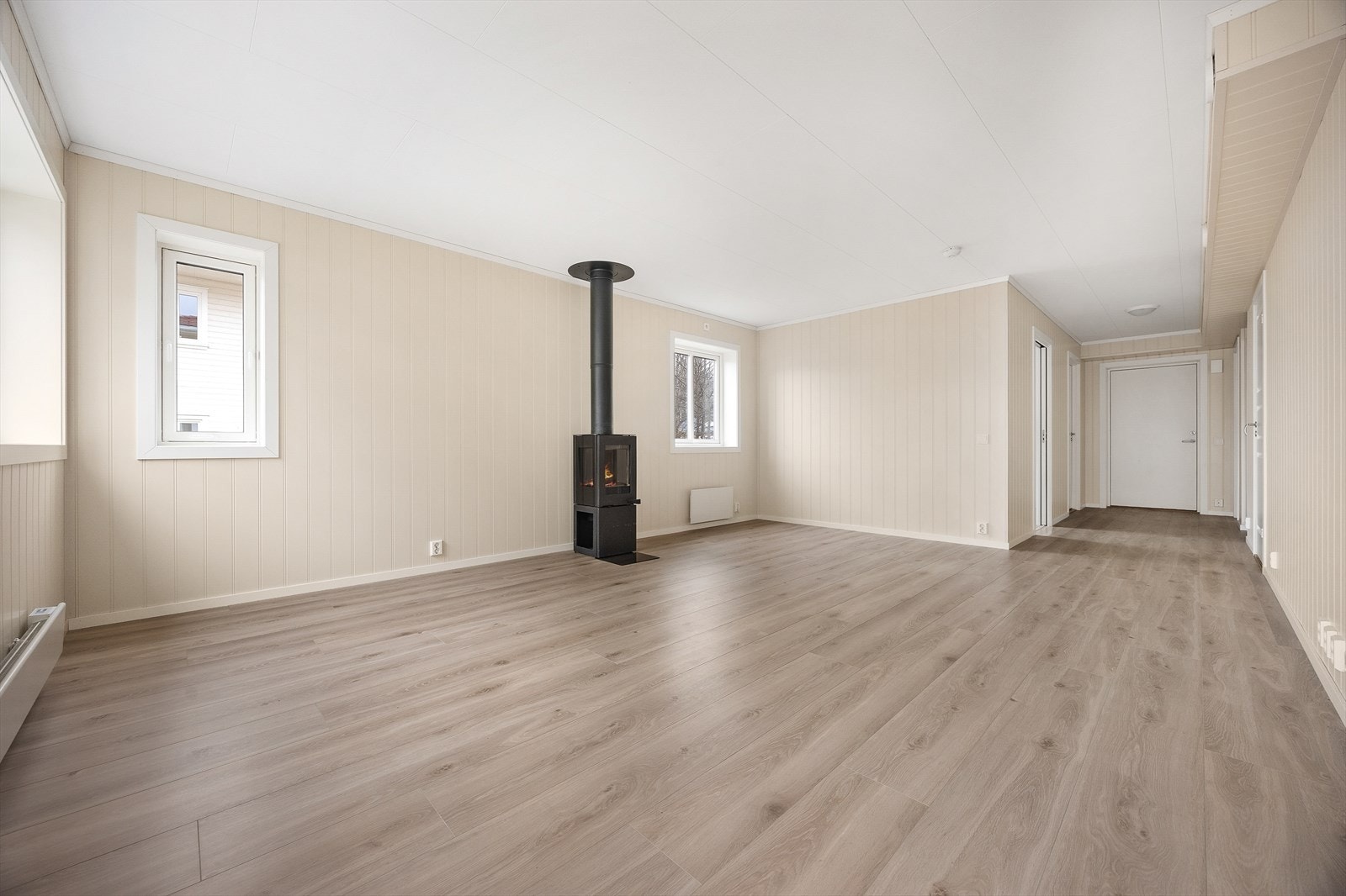 Gjennomgående laminatgulv og lyse, malte veggplater skaper en helhetlig og innbydende atmosfære. Galleribilde