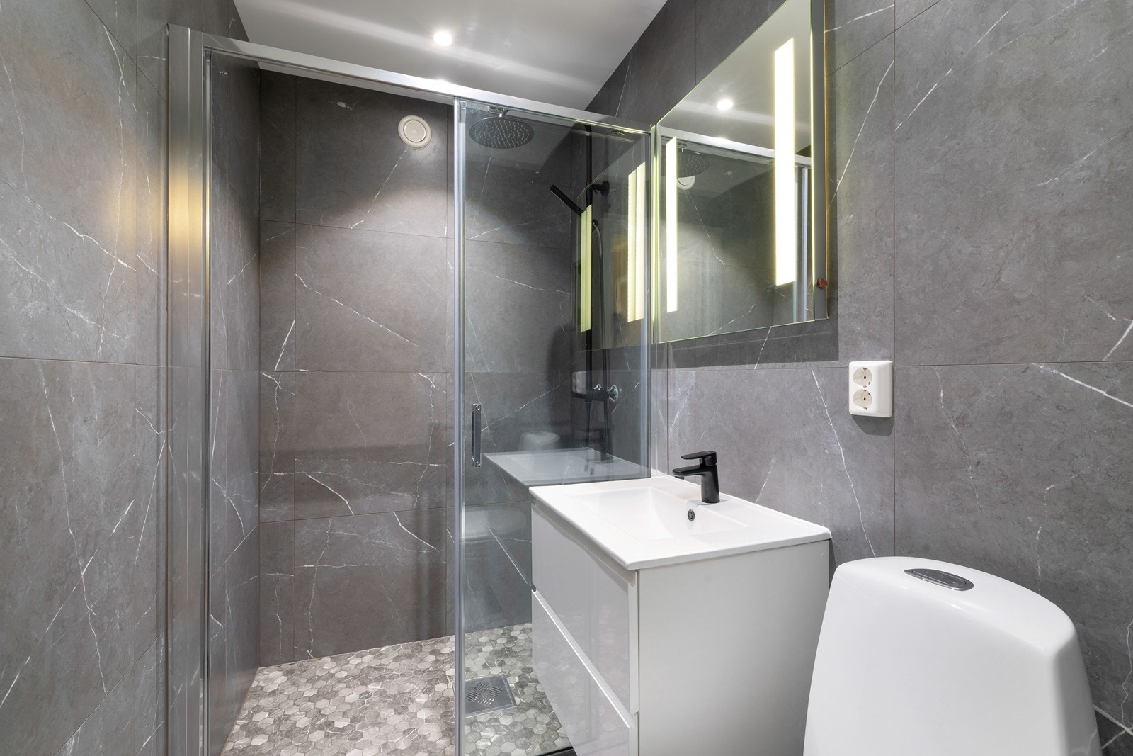 Nyere pent bad fra 2022 med dusjhjørne, servant med underskuffer og toalett. Galleribilde