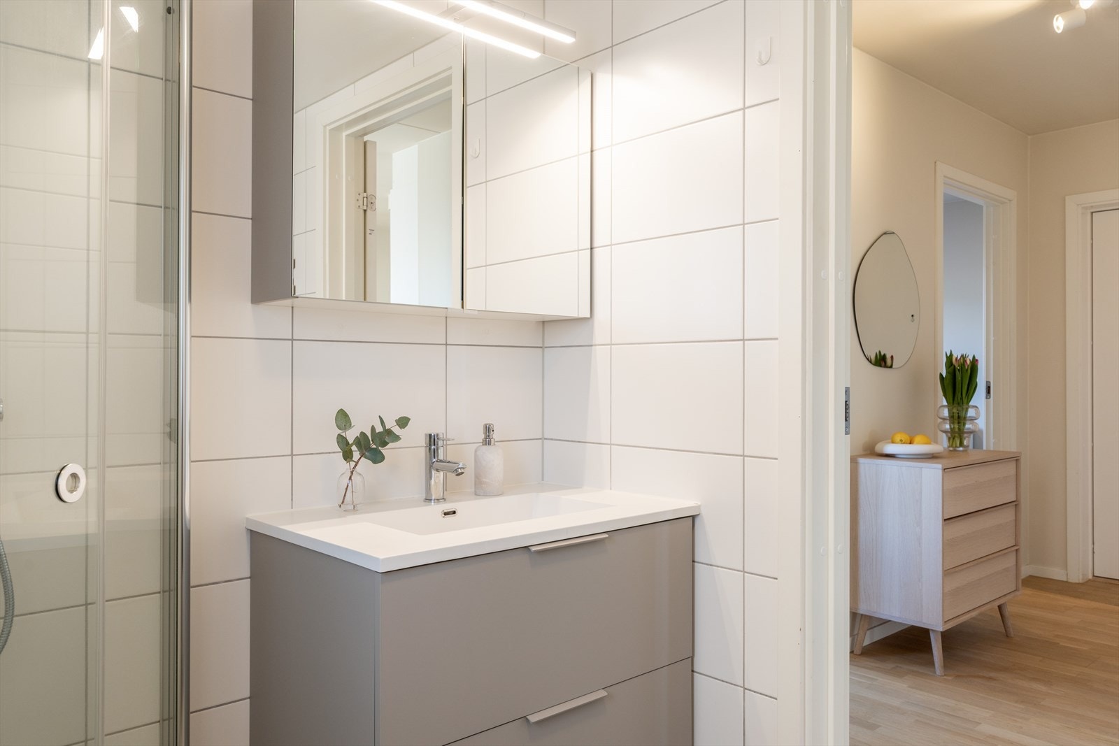 Badet er innredet med vegghengt toalett, servant med innredning, speilskap m/lys og dusjhjørne med svingbare glassdører. Galleribilde