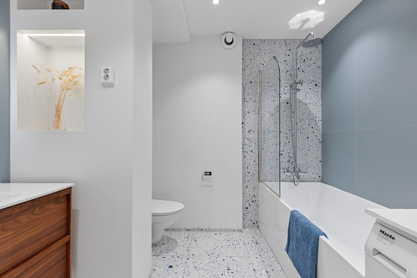 En dekorativ nisje med belysning skaper en elegant oppdeling mot toalettsonen. Det er registrert avvik i fallforholdene mot sluk sammenlignet med kravene på byggetidspunktet. Galleribilde