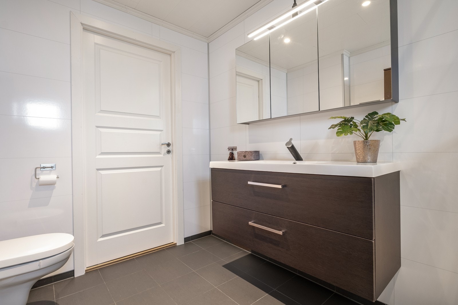 Tidsriktig, mørk baderomsinnredning og speilskap med overbelysning. Galleribilde