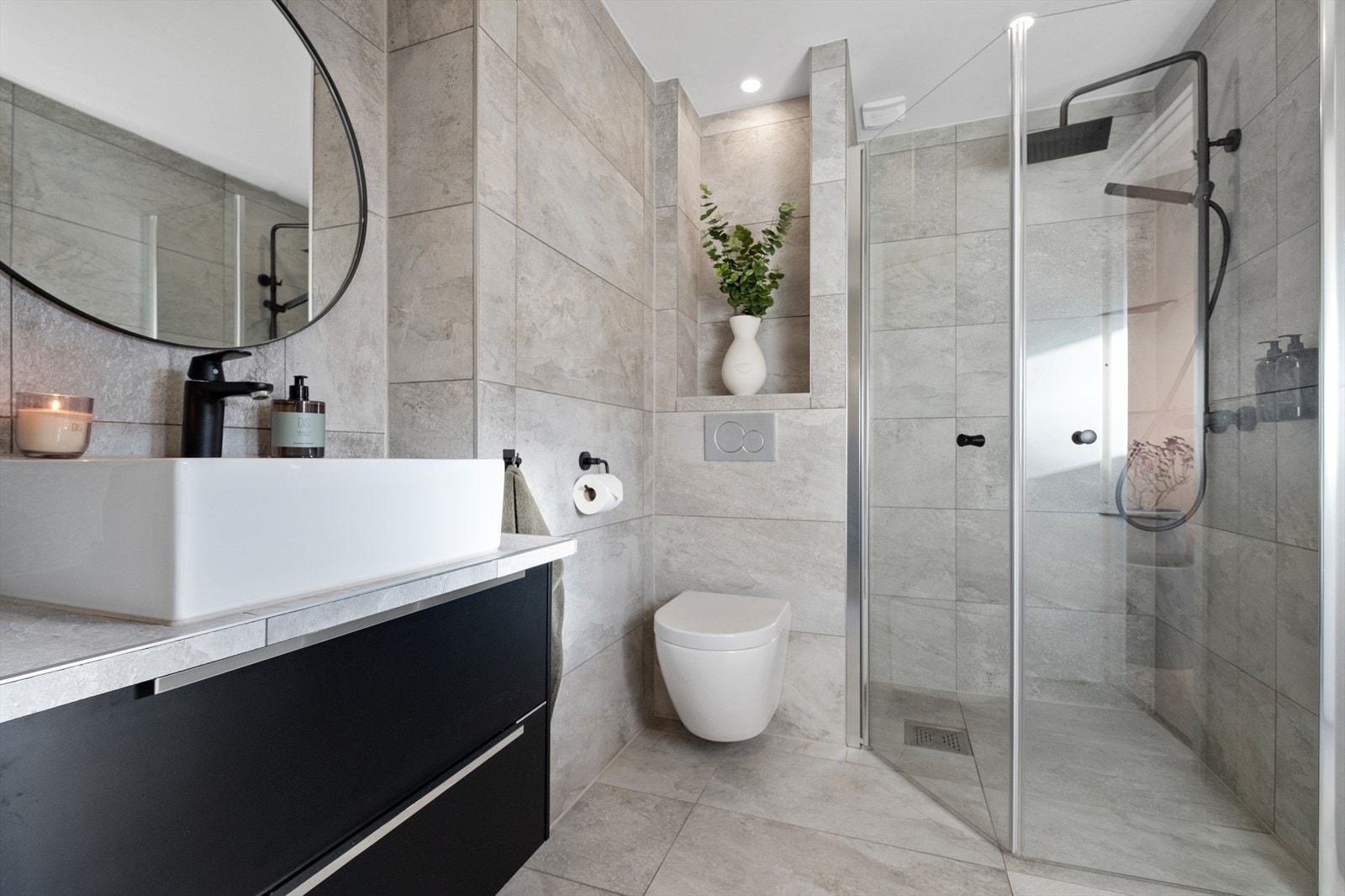 Badet er utstyrt med dusjhjørne, veggmontert toalett, servantskål med underskap og elektrisk avtrekk. Galleribilde