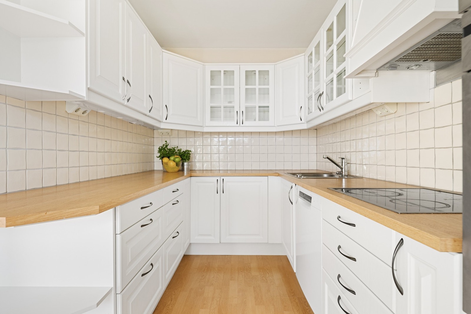 Lys kjøkkeninnredning med malte, profilerte fronter, laminat benkeplate og fliser mellom benkeplate og overskap. Det er integrert stekeovn, keramisk topp og mikrobølgeovn. Opplegg for oppvaskmaskin Galleribilde