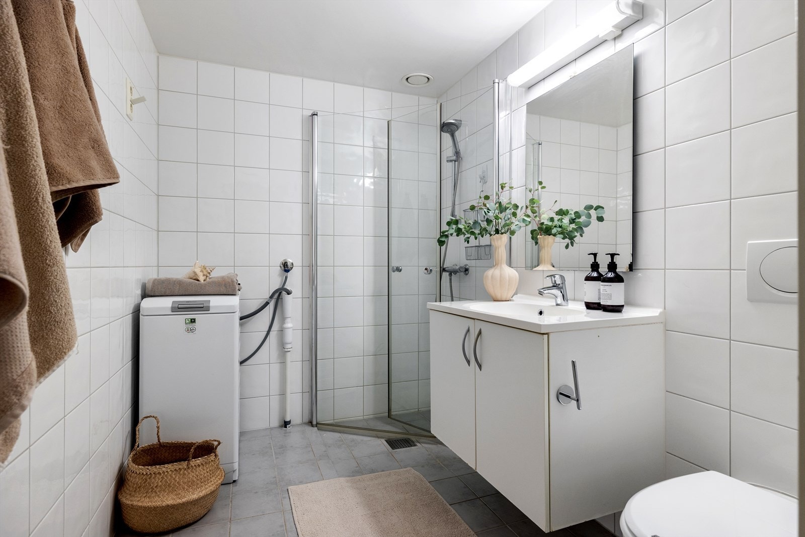 Badet har flislagte overflater, elektriske varmekabler i gulvet, vegghengt toalett og opplegg for vaskemaskin. Galleribilde