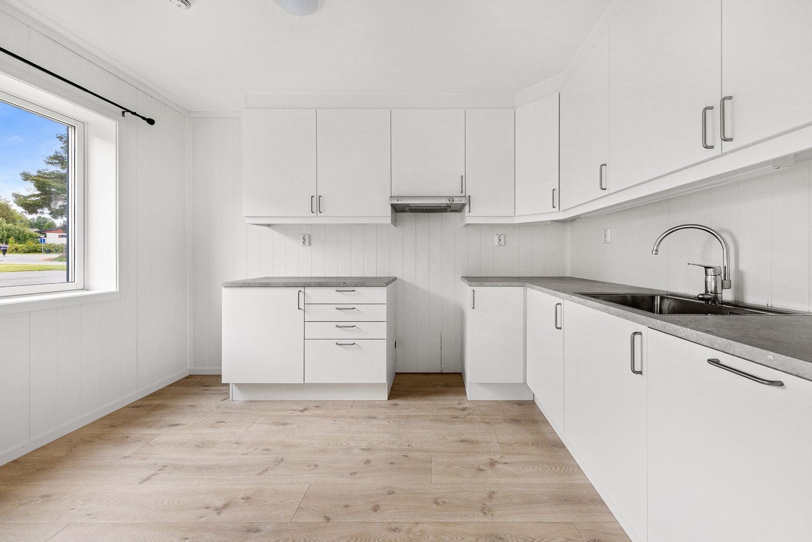 Kjøkkenet har en lys og tidløs innredning med glatte fronter og benkeplate i laminat, samt avsatt plass til hvitevarer. Galleribilde