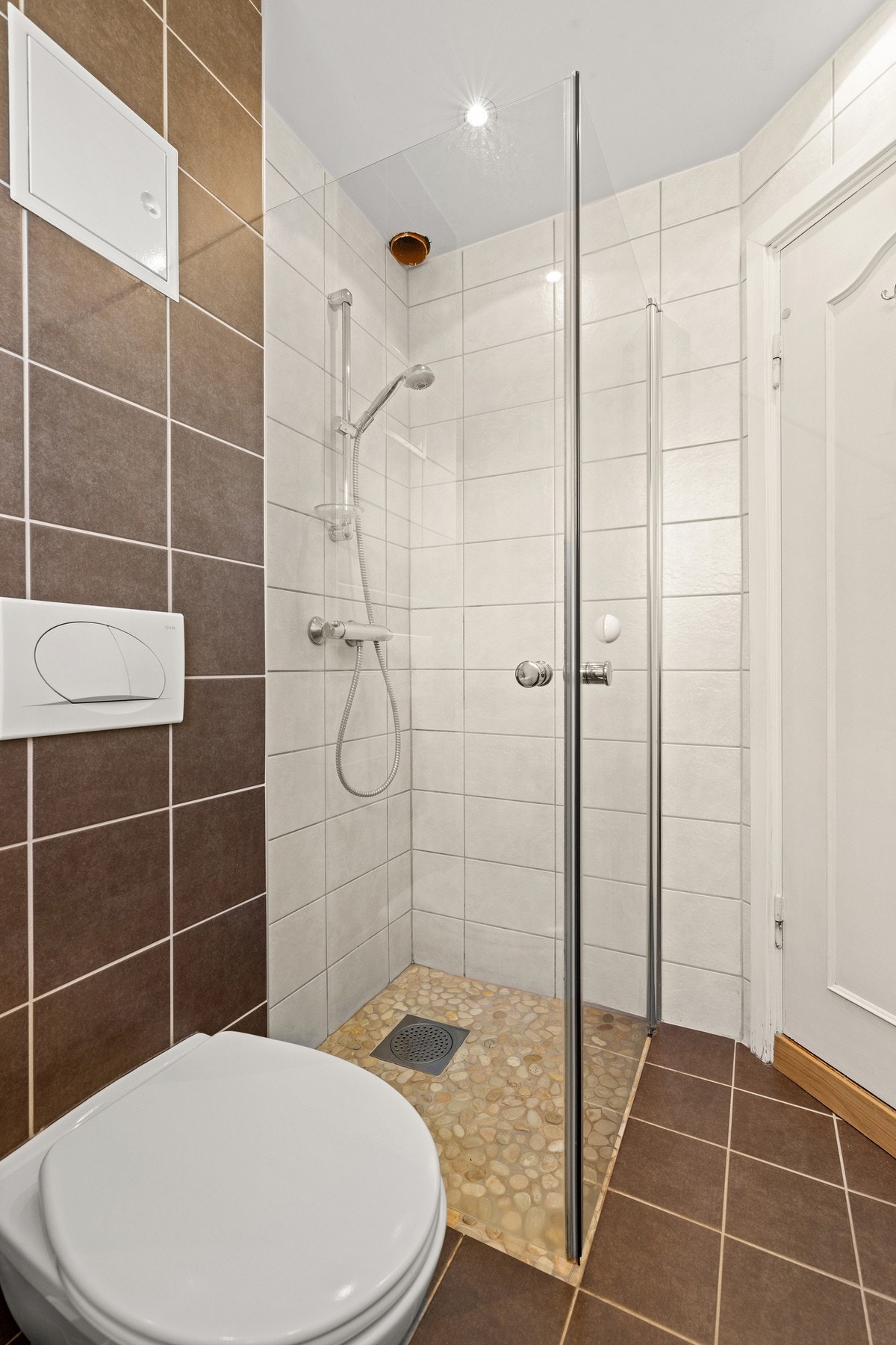 Badet er innredet med servant med skuffeseksjon, veggmontert toalett og dusjhjørne med innfellbare glassdører. Galleribilde