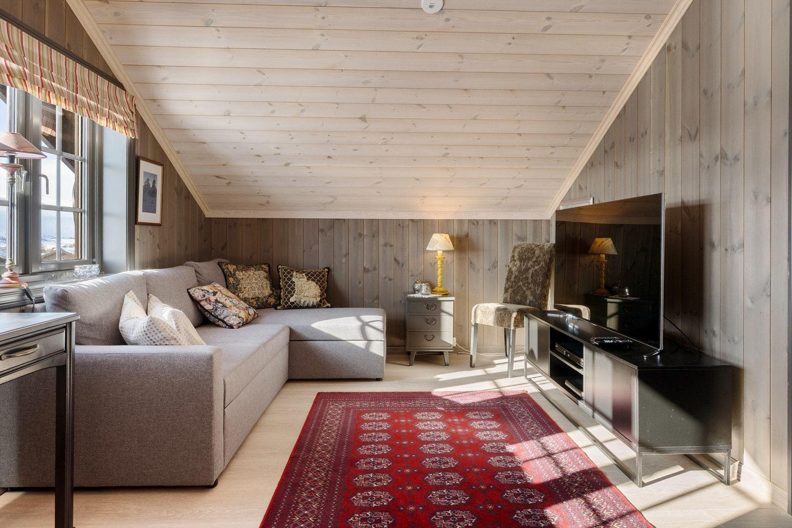 Velkommen opp. Her er det en loftstue med laminatgulv og fabrikkbeiset panel på vegger og i tak. Galleribilde