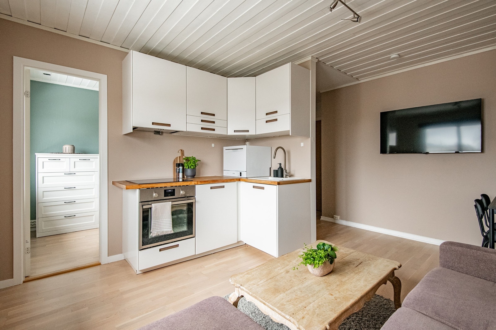 Kjøkkenet har en pen og moderne innredning med hvite, slette fronter og en benkeplate i treverk som gir en varm og naturlig kontrast til det øvrige interiøret. Galleribilde