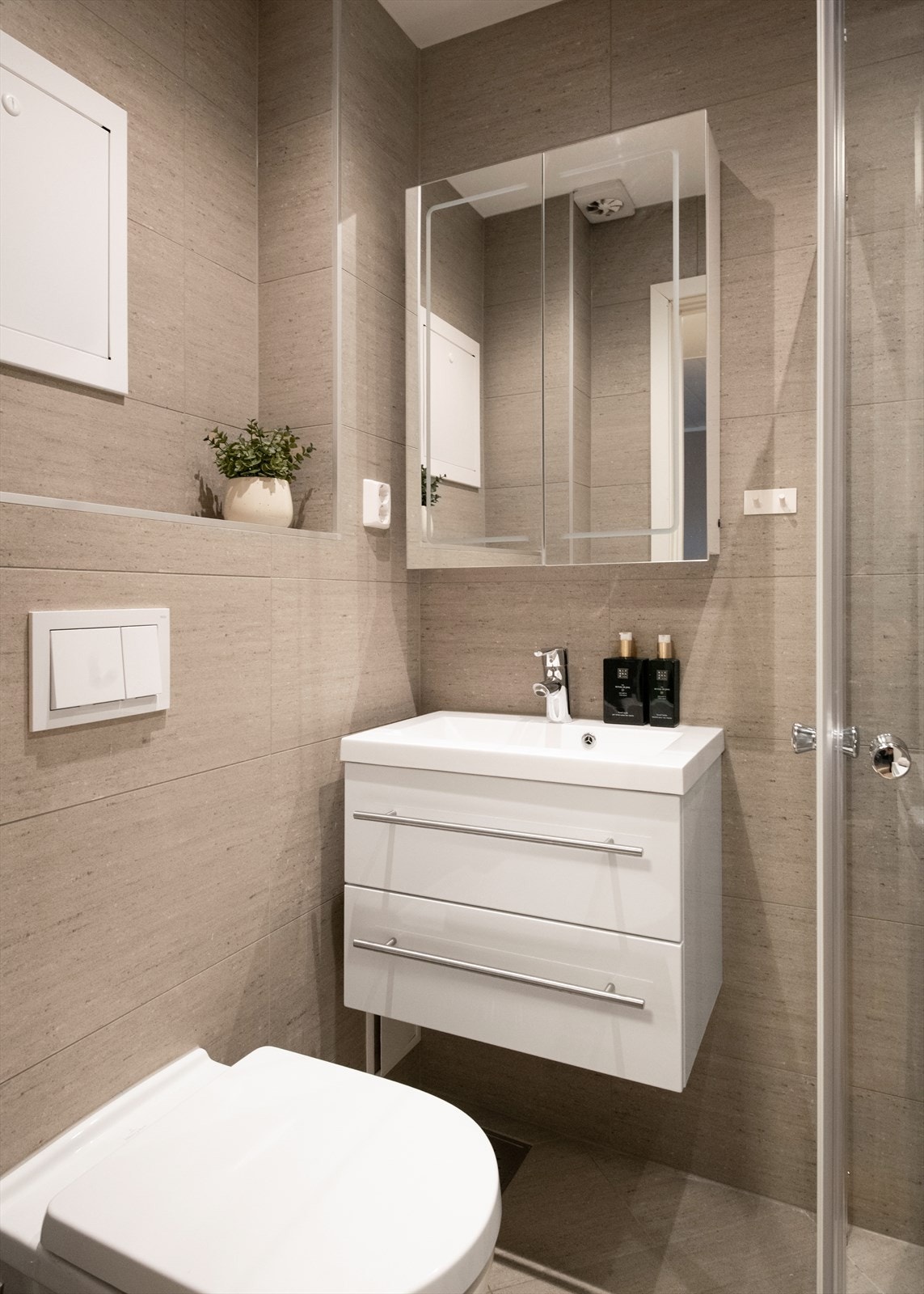 Baderomsinnredningen inkluderer servant med skuffer, et speilskap med integrert lys, vegghengt toalett, samt et dusjhjørne med glass-skyvedører. Galleribilde