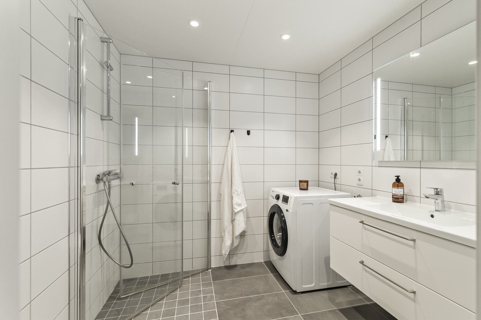 Badet er delikat og moderne, helfliset med store, hvite fliser på veggene og mørke fliser på gulv. Galleribilde