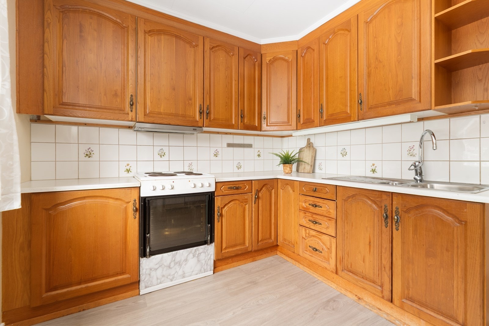 Romslig kjøkken med eldre, takhøy kjøkkeninnredning. Innredningen har godt med skapplass og profilerte fronter. Galleribilde