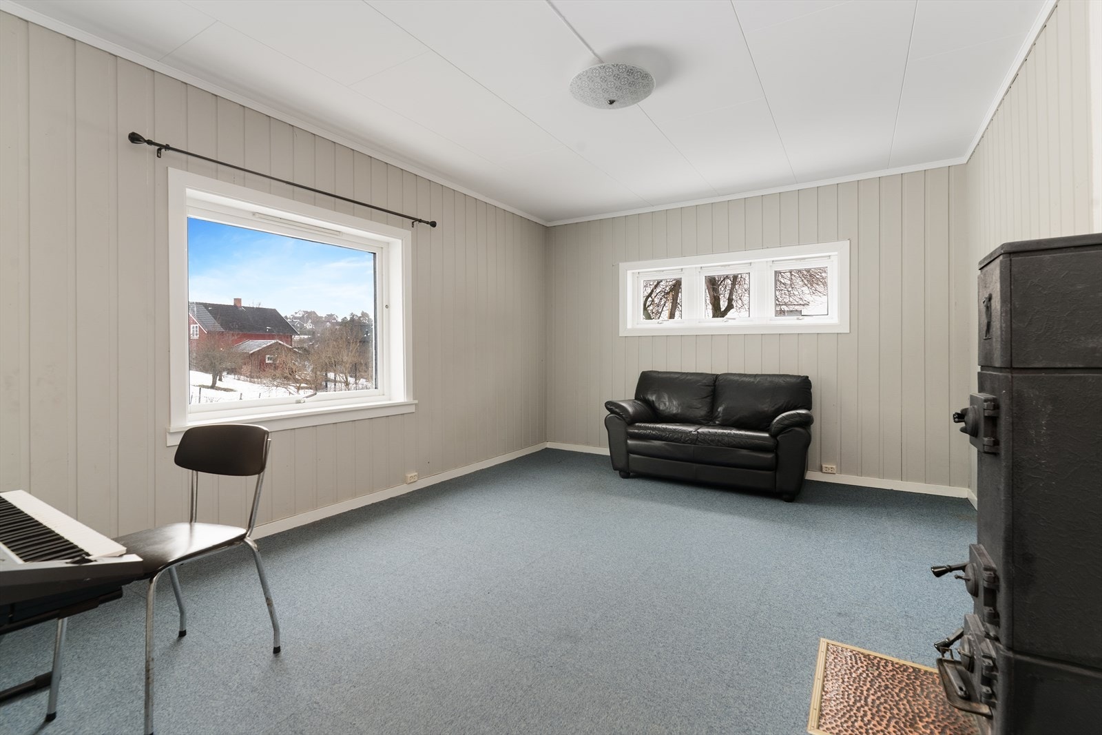 Det ene soverommet i underetasjen er stort og fremstår i dag som en kjellerstue. Her er det eldre vedovn for oppvarming. Galleribilde