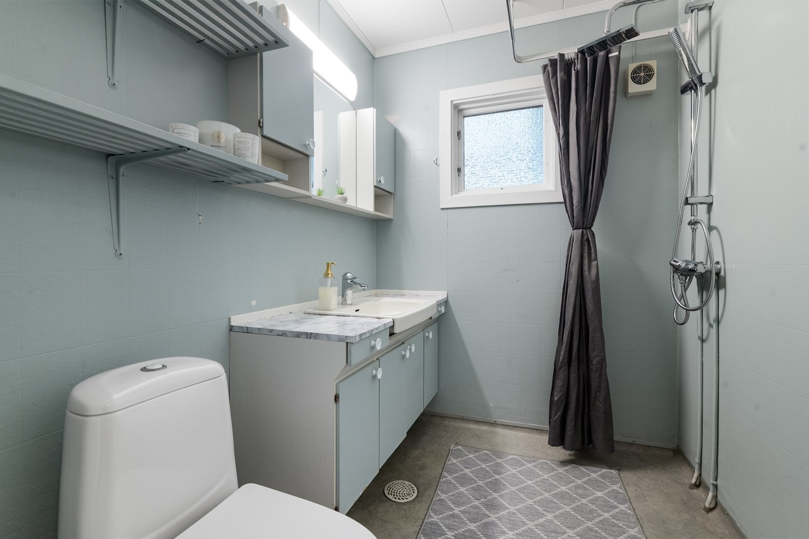 Eldre bad i hovedetasjen med gulvmontert toalett og dusj på vegg. Romslig servantskap med benkeplate og nedfelt vask. Galleribilde