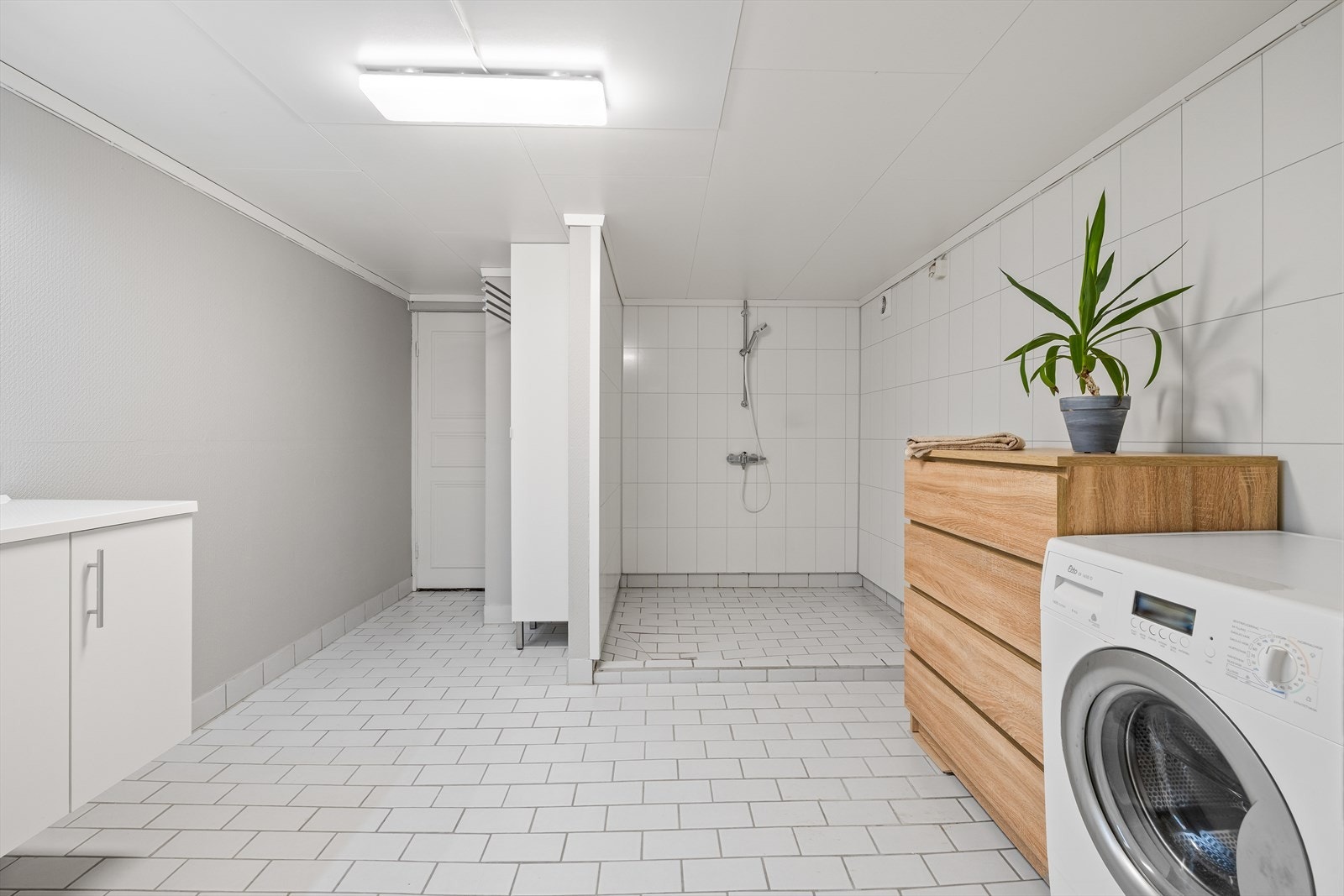 Badet i kjelleren er flislagt med nedfelt servant, dusjhørne og opplegg for vaskemaskin Galleribilde