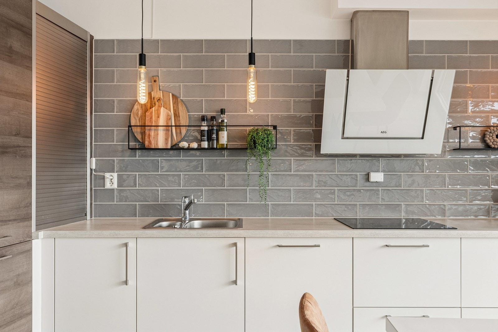 De grå flisene, de åpne hyllene og de gjennomtenkte belysningspunktene skaper både funksjonalitet og en stilren estetikk. Galleribilde