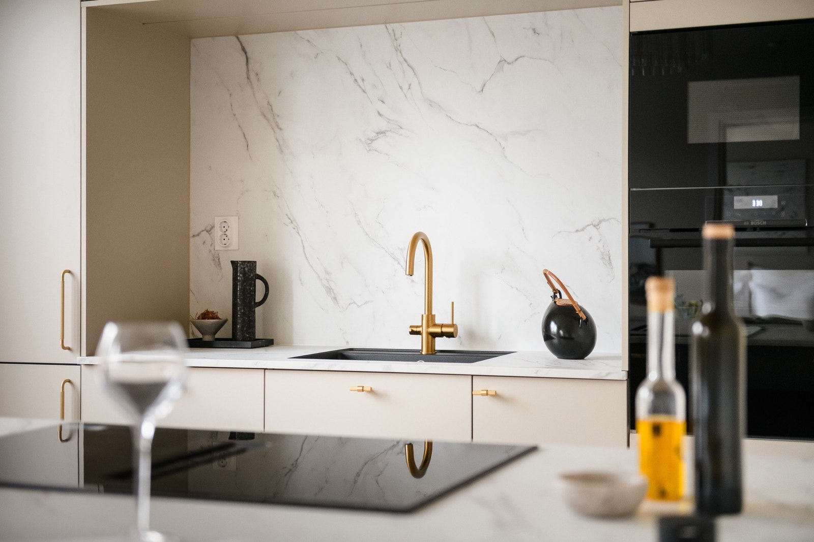 Stilrent HTH-kjøkken med marmorert bakplate, pop-up stikkontakt og lekkert armatur i børstet messing. Galleribilde