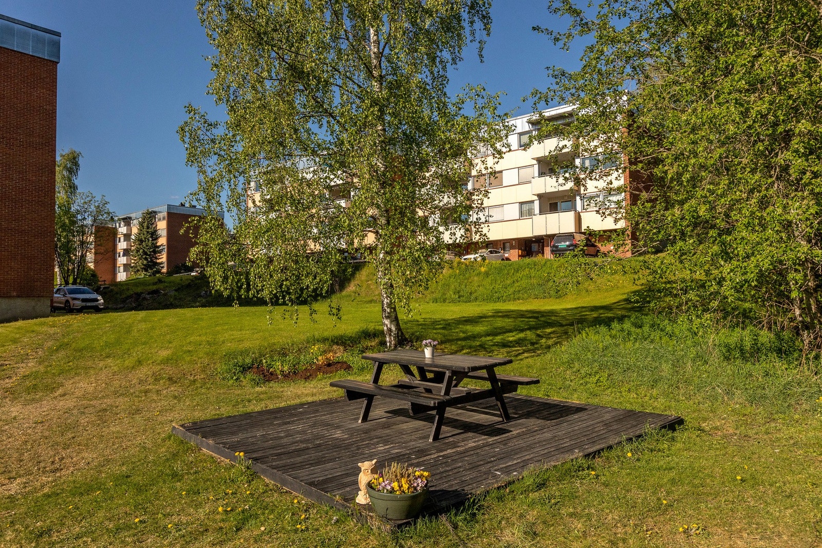 Felles tomt for borettslaget som består av en asfaltert gårdsplass og grøntarealer. Galleribilde