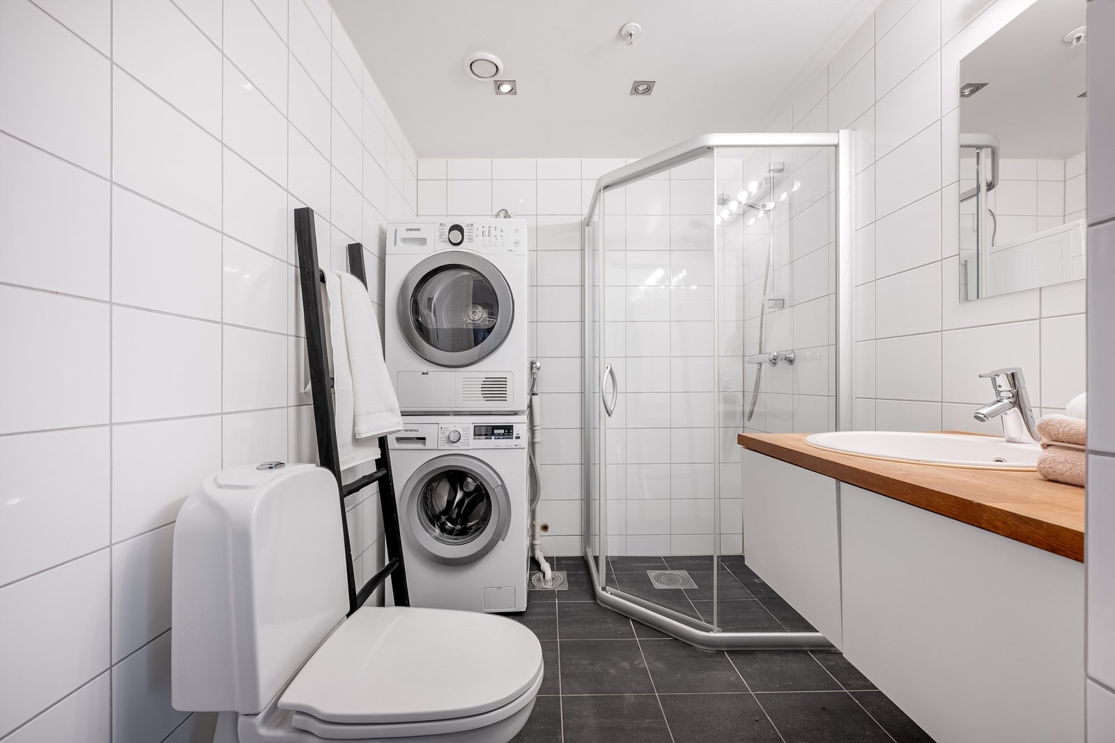 Fint helfliset bad av godt størrelse med varme i gulv. Det er dusjhjørne, toalett og servant med oppbevaringsplass i skuffer. Stort speil på vegg. Opplegg for vaskemaskin samt plass til tørketrommel om man skulle ønske det. Et fint og stilrent baderom. Galleribilde
