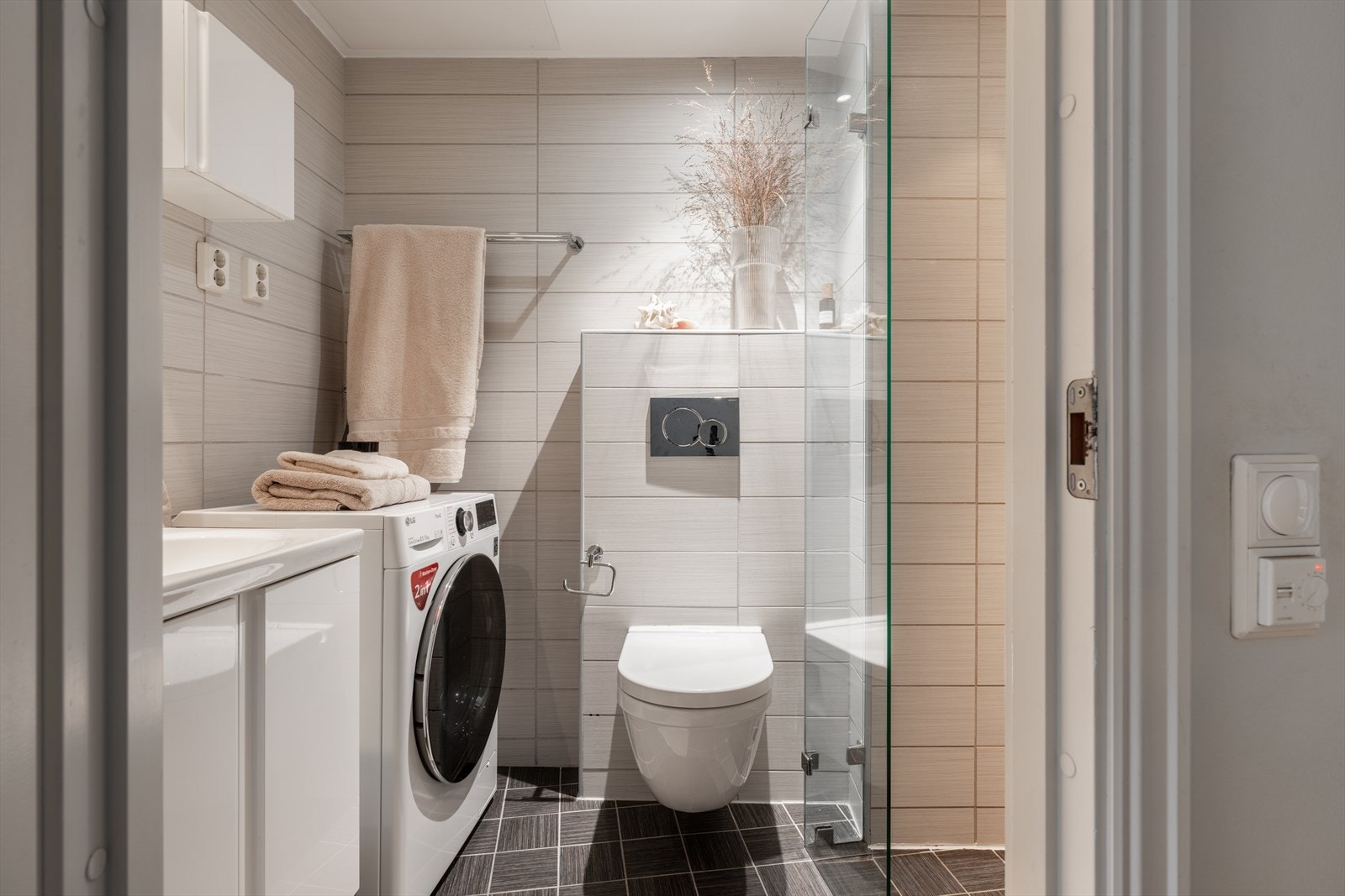 Moderne, flislagt bad med elektrisk gulvvarme, vegghengt toalett og opplegg for vaskemaskin. Galleribilde