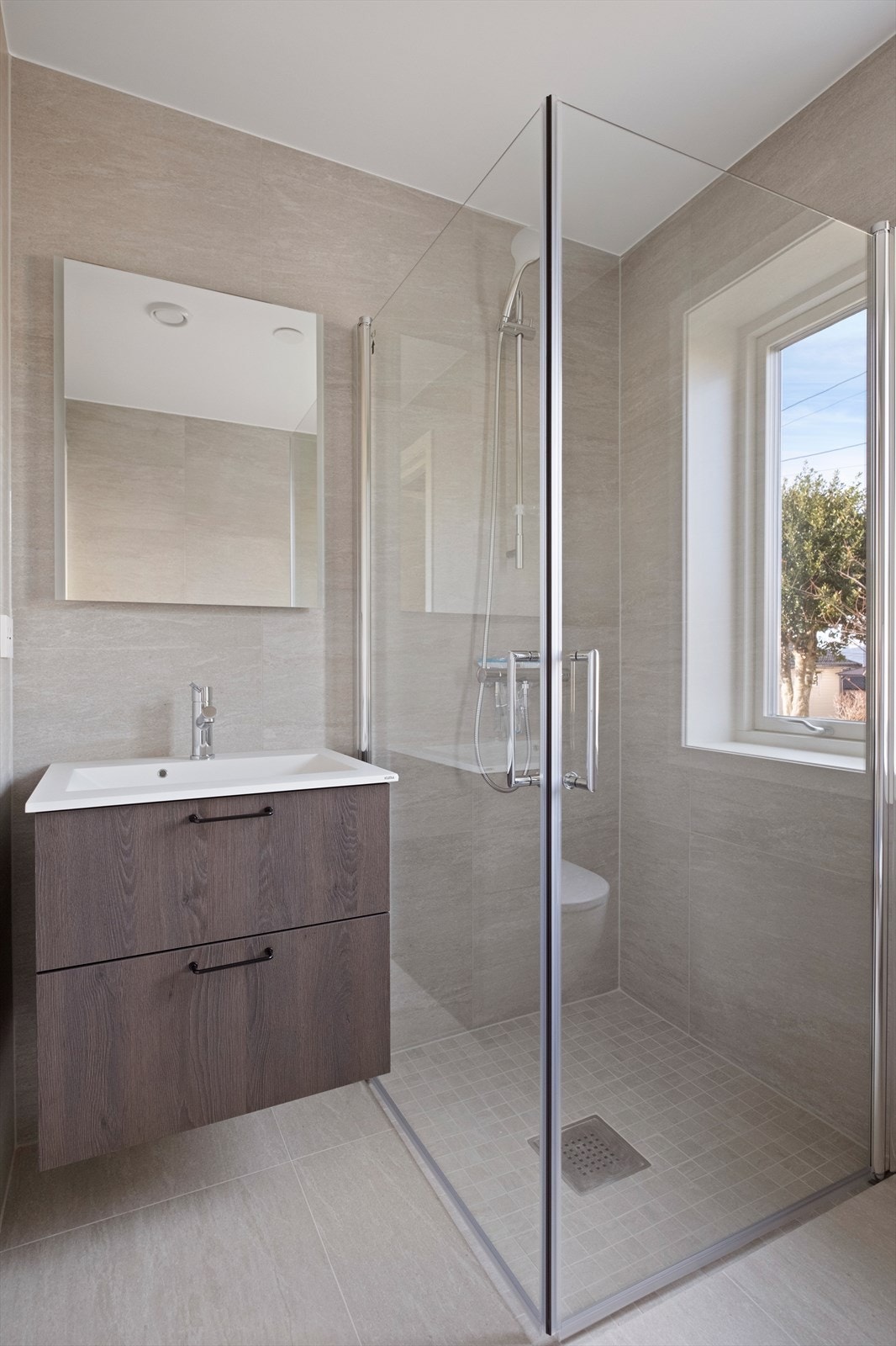 Badet har dusjdører, vegghengt WC og innredning med servant. Galleribilde