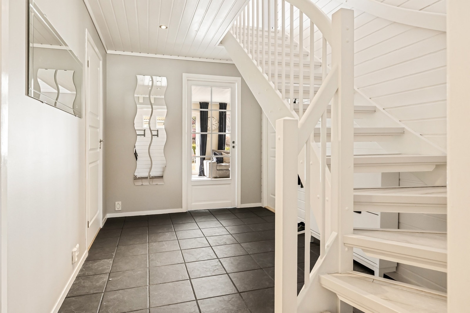 Gangen ønsker velkommen med flislagt gulv og trapp opp til andre etasje. Døren i glass slipper lyset gjennom fra stuen. Galleribilde