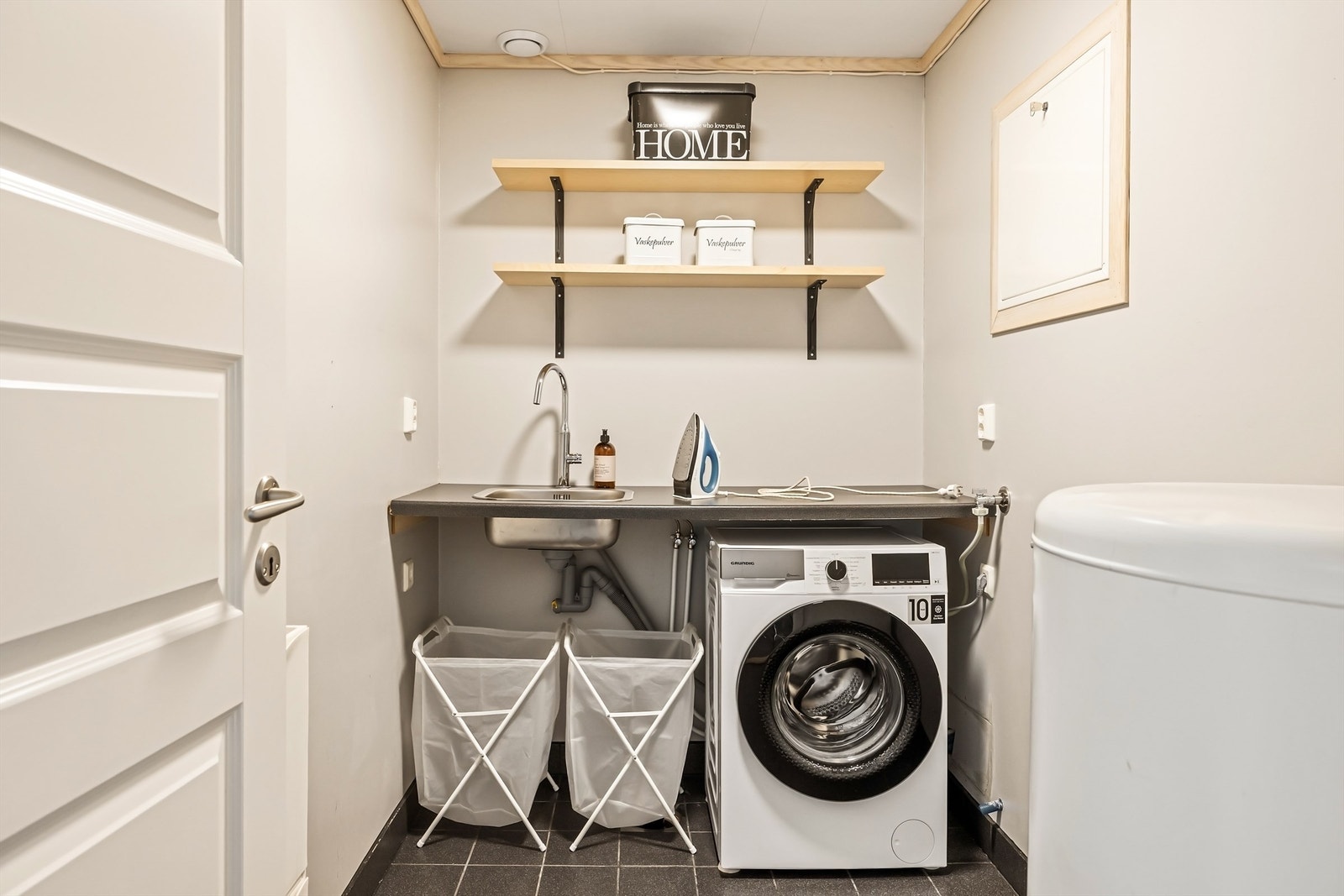 Praktisk vaskerom med flislagt gulv med varmekabler, opplegg for vaskemaskin og utslagsvask. Galleribilde