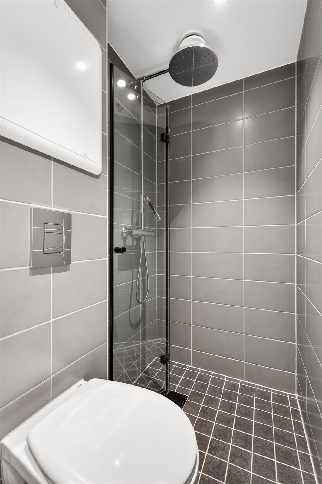 Baderommet inneholder dusjhjørne med innfellbare glassdører, servantskap, vegghengt toalett og opplegg for vaskemaskin. Galleribilde