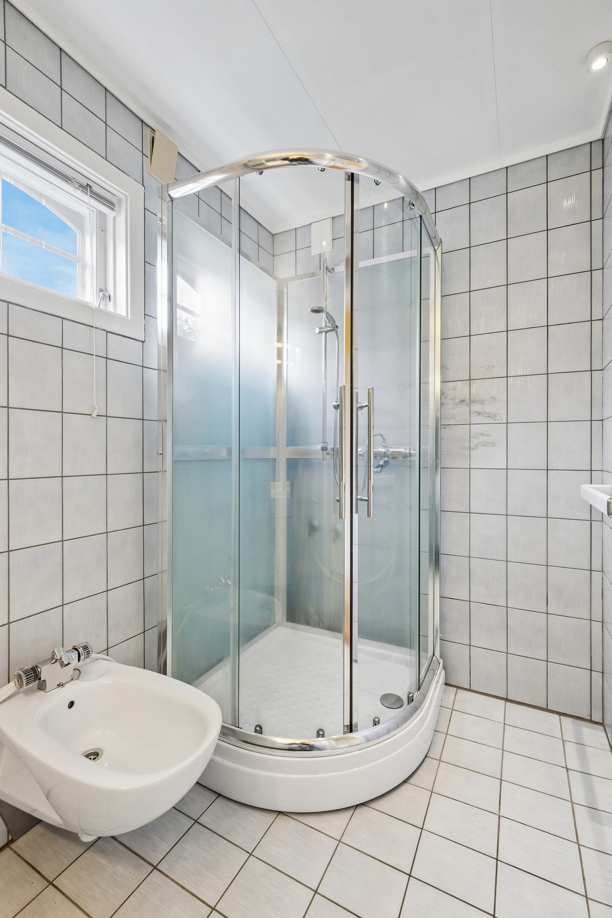 Flislagt bad med dusjkabinett og vindu som gir naturlig lys. Galleribilde