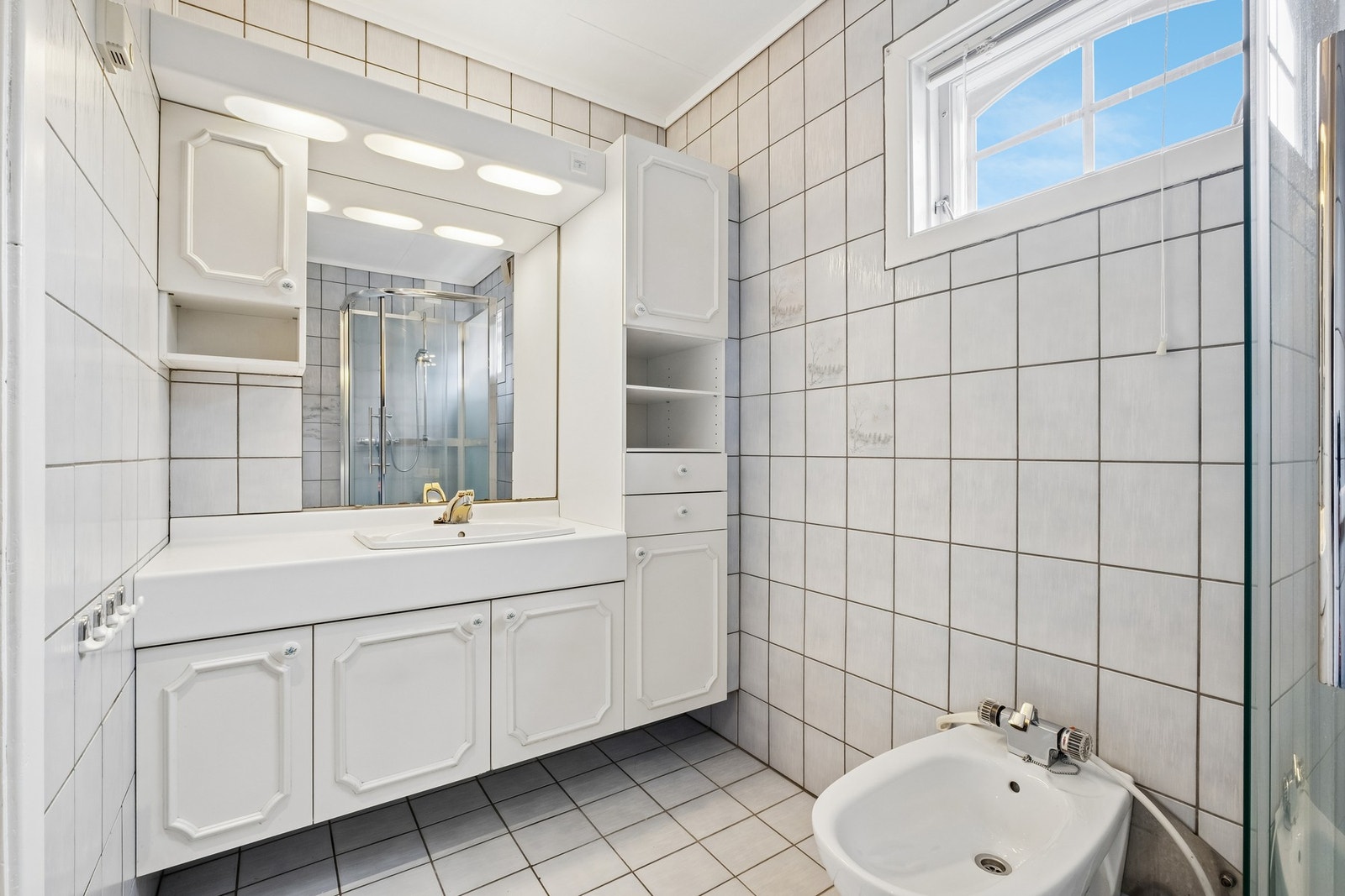 Badet har flislagte vegger og gulv, speil med innfelte lys og dusjkabinett. Galleribilde