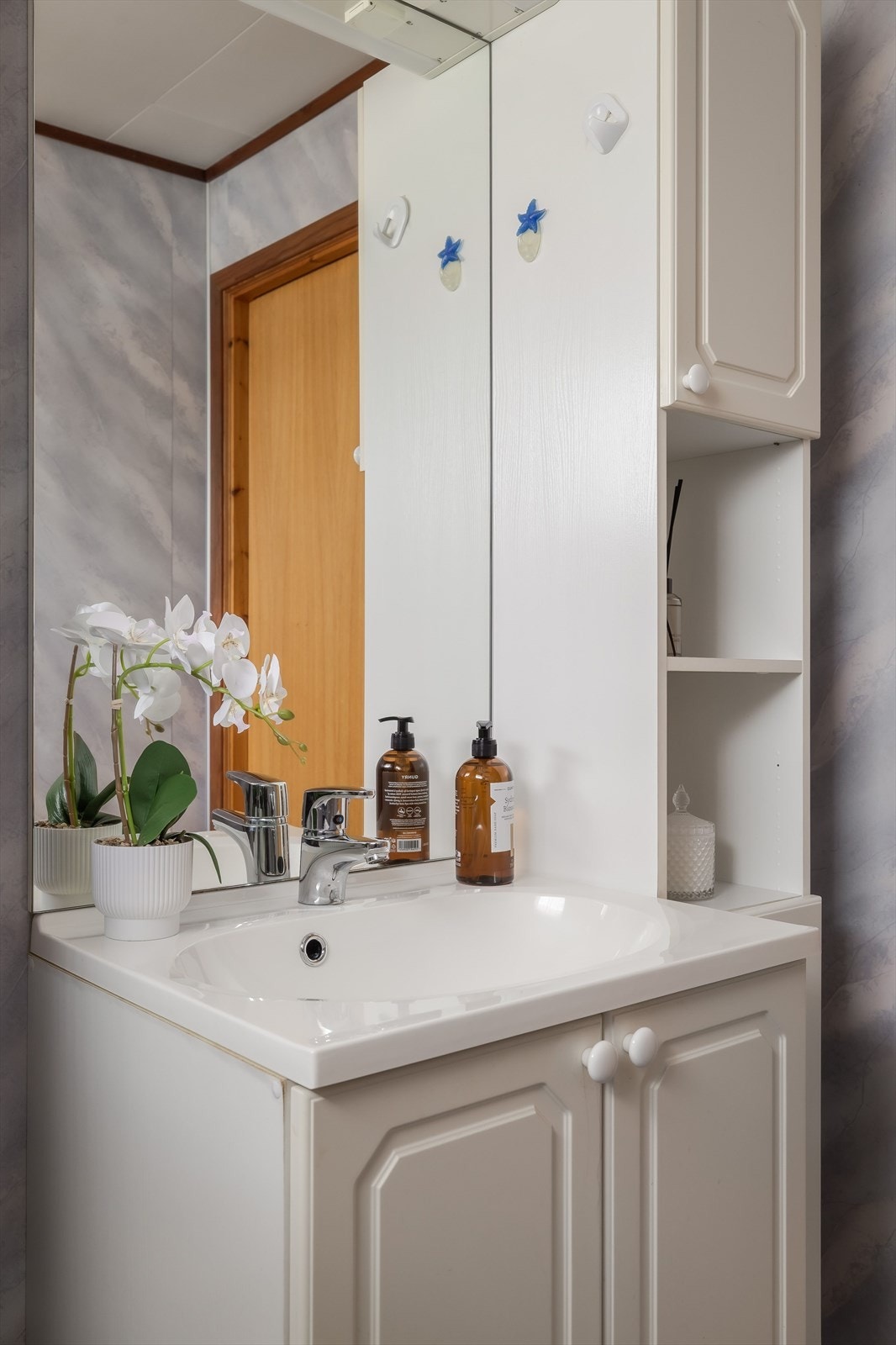 Baderomsinnredning med underskap og heldekkende servant. Over servanten er det speil, lys og elektrisk uttak. Veggskap ved siden av. Galleribilde