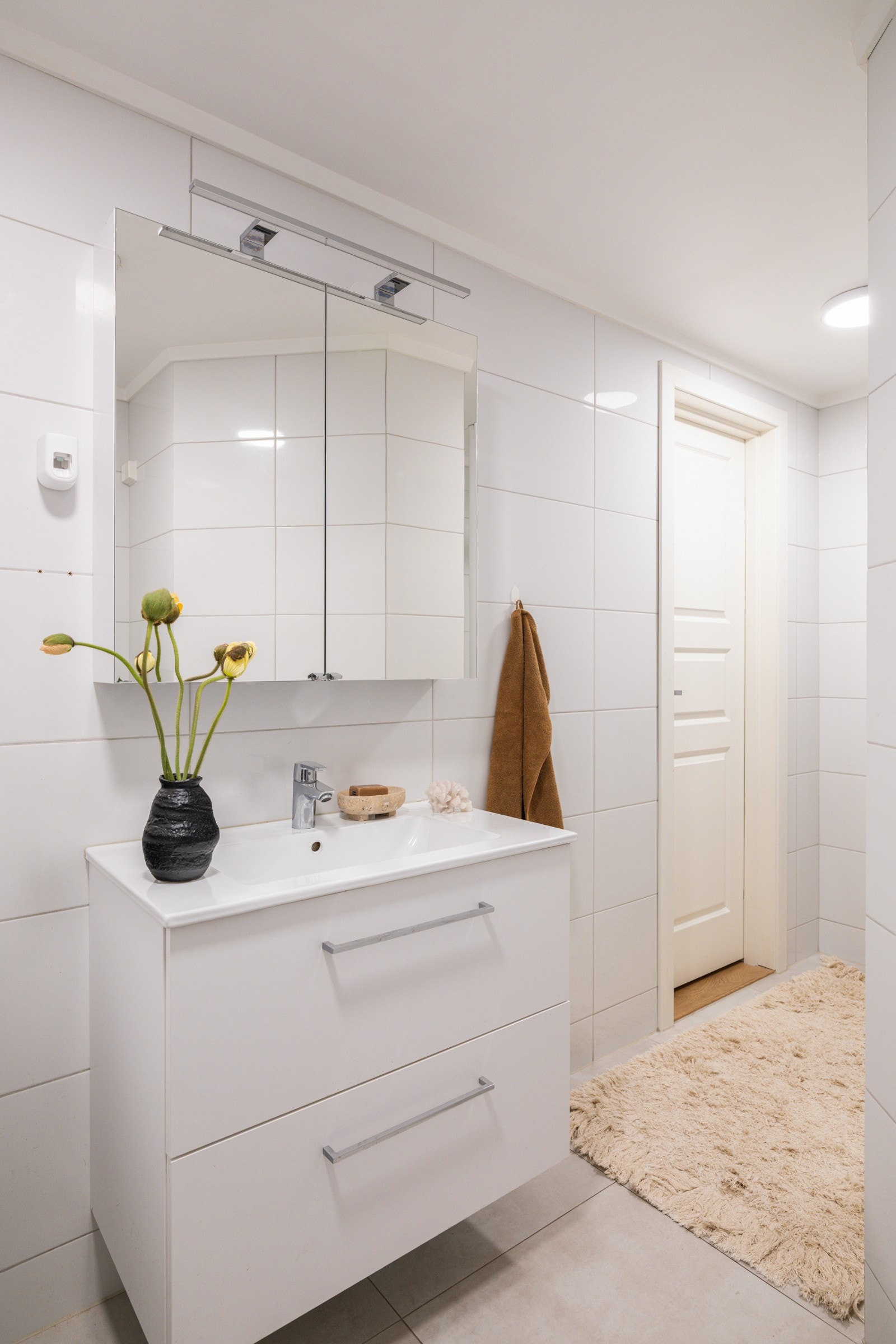 Moderne baderomsinnredning med skuffer og heldekkende servant, speilskap med belysning over. Galleribilde