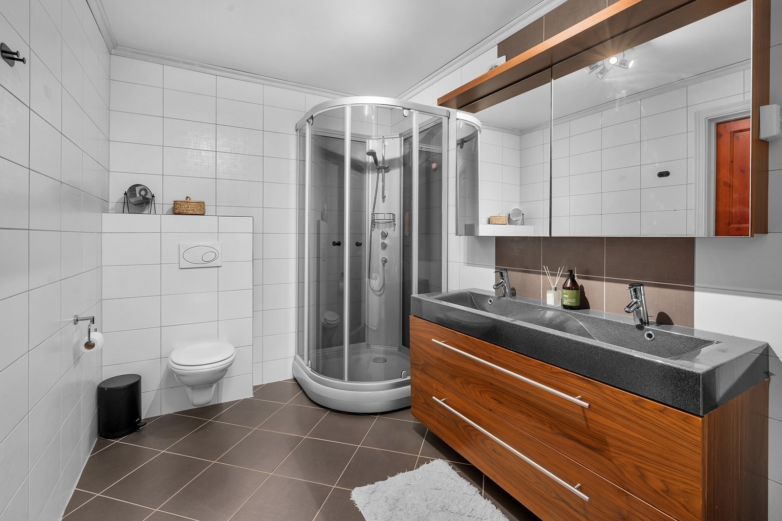 Flott flislagt bad i gulv og vegger. I gulv er det elektriske varmekabler. Rommet har vegghengt toalett, dusjkabinett og praktisk dobbelt servant. Galleribilde