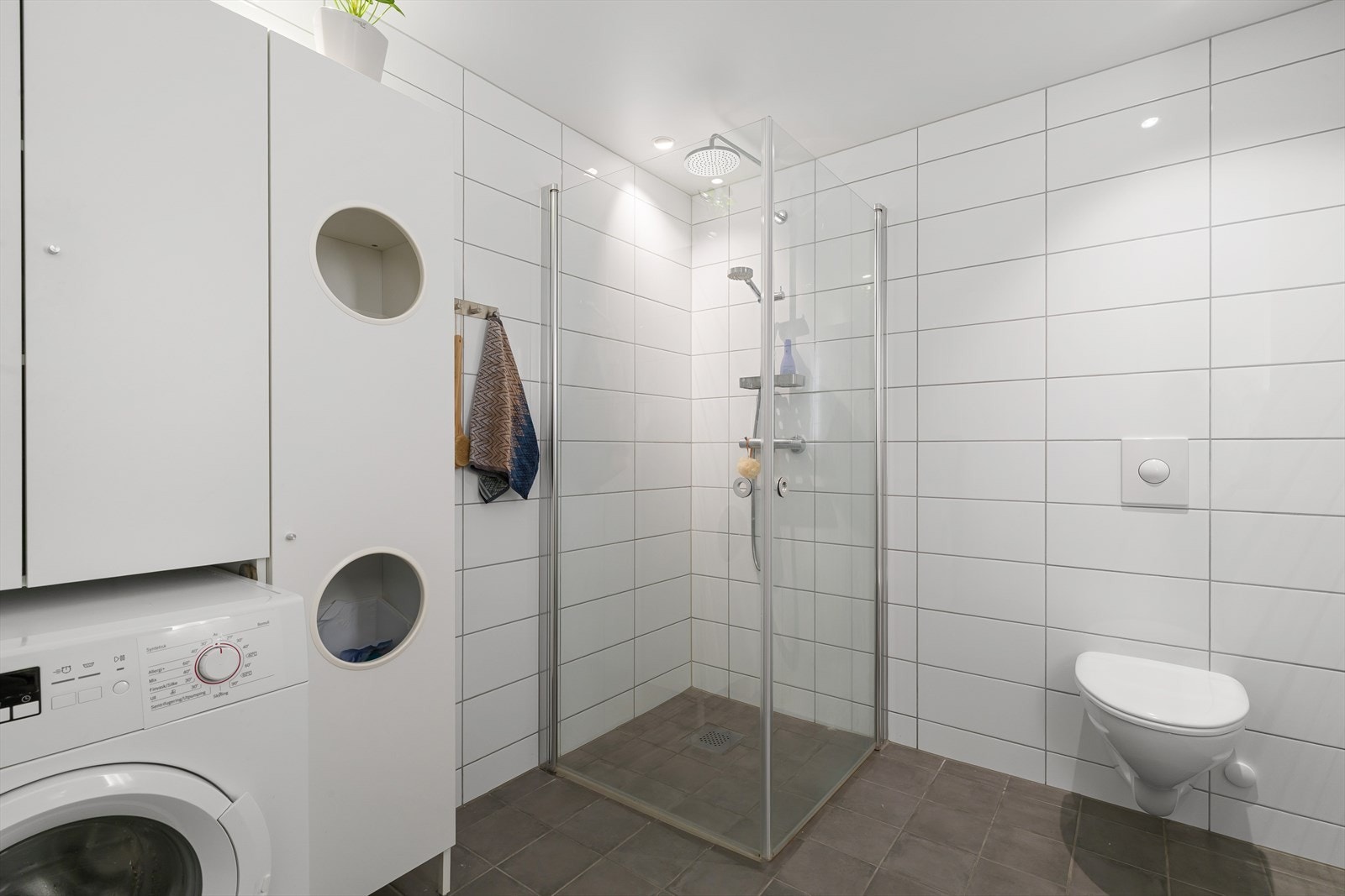 Praktisk baderom med integrert opplegg for vaskemaskin og gode oppbevaringsløsninger. Galleribilde