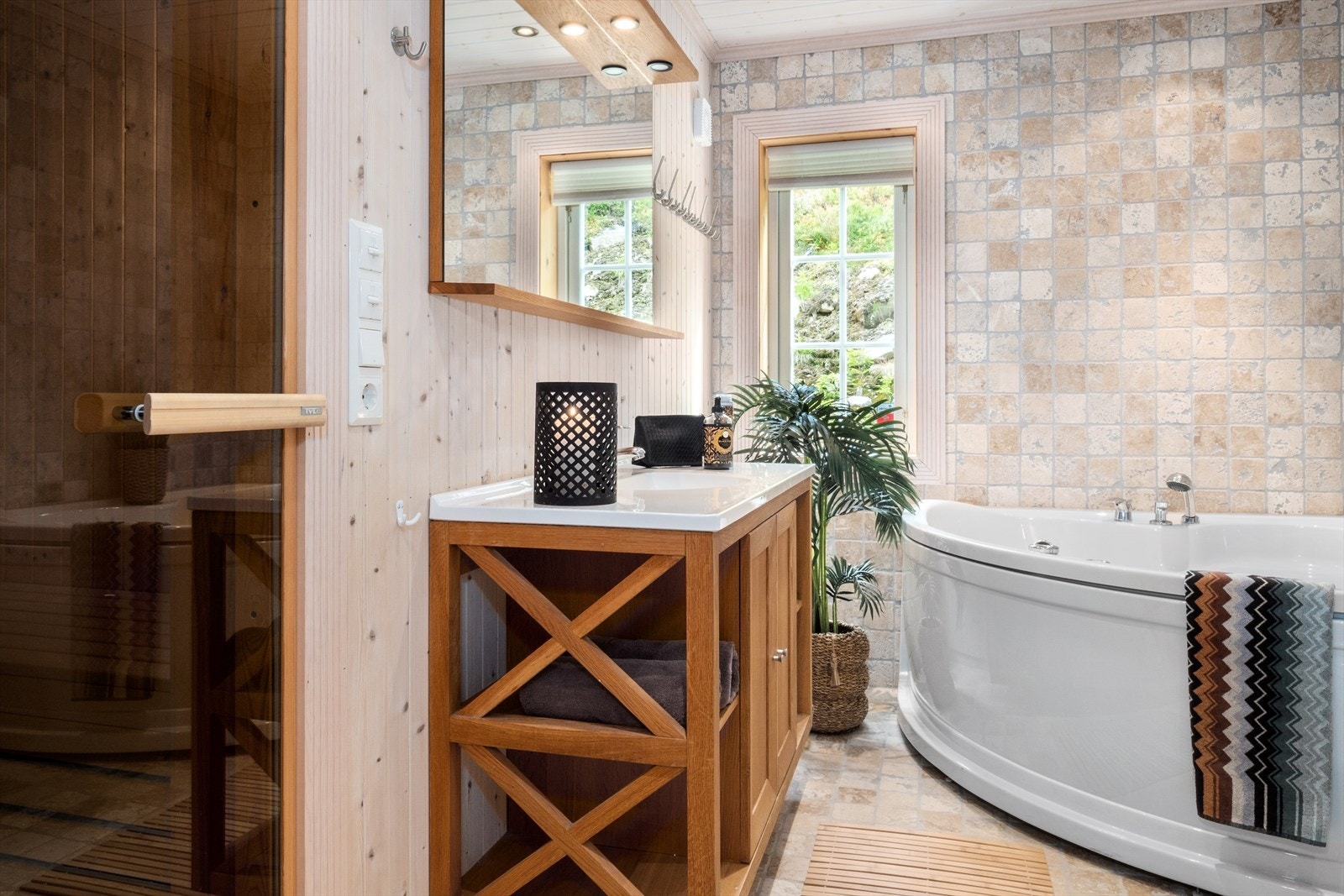 Baderommet i første etasje er romslig og har lyse fliser på gulv og vegg. Badet inneholder dusjhjørne med innfellbar dør i glass, stort boblebadekar, servant, speil og belysning, samt gulvstående toalett. Galleribilde