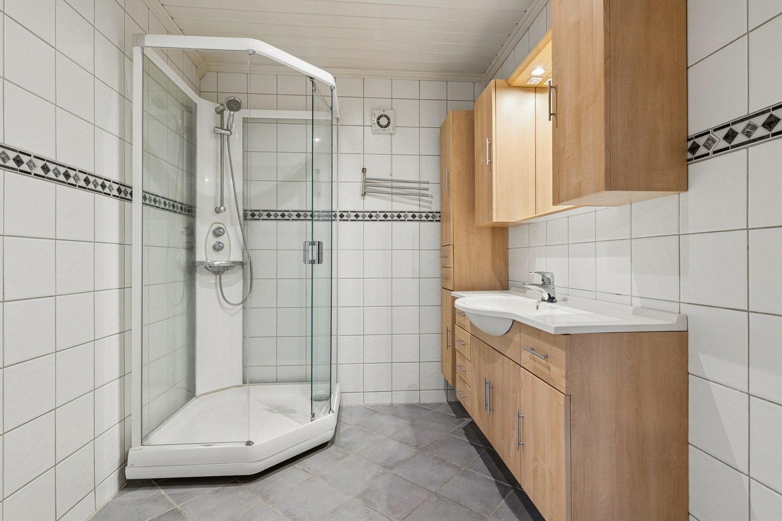 Pent flislagt bad utstyrt med dusjkabinett og en romslig baderomsinnredning. Galleribilde