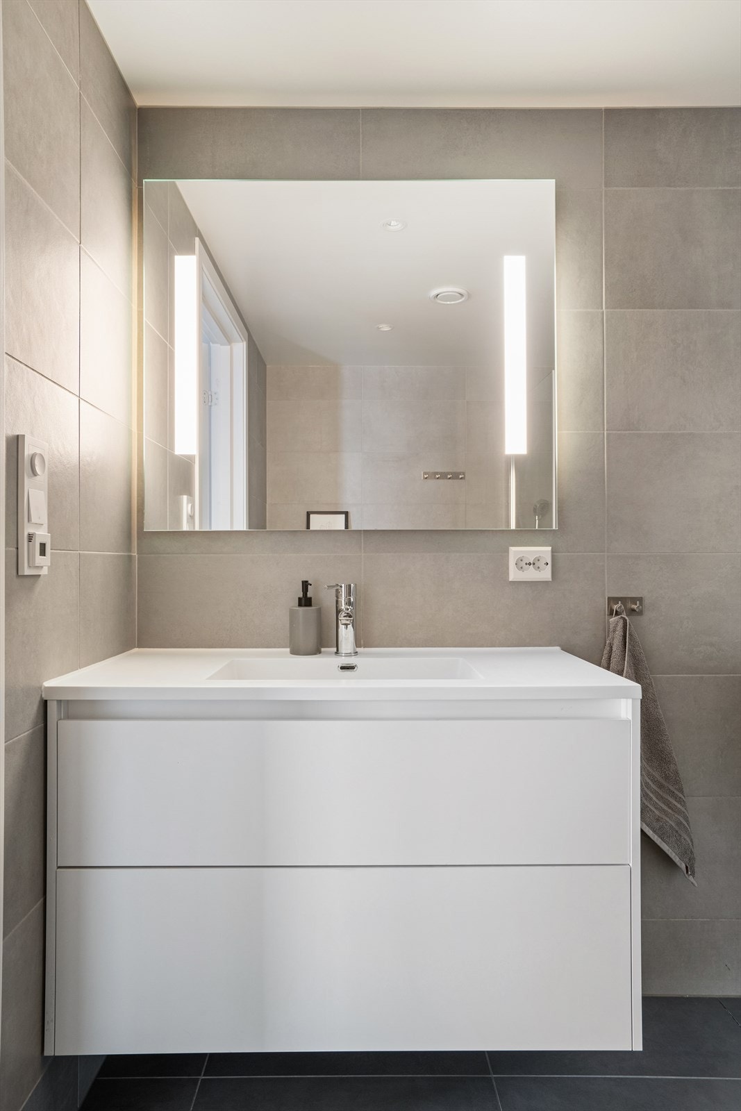 Servant med speilbelysning og veggmontert toalett gir funksjonell innredning på badet. Galleribilde