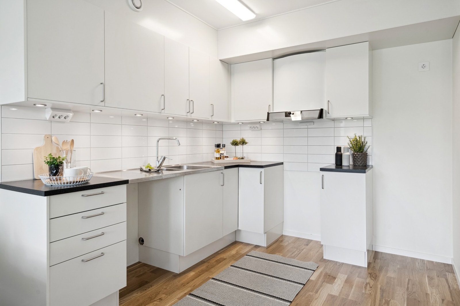 Kjøkkeninnredningen har hvitmalte, glatte fronter og laminatbenkeplate. Det er avsatt plass til hvitevarer og belysning under overskapene. Galleribilde