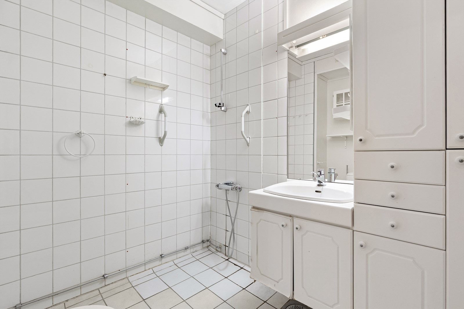 Badet har fliser på golv, delvis flis og måla våtromsbelegg/plater på veggar. Rommet er utstyrt med toalett, dusjhjørne og servant med innredning. Galleribilde