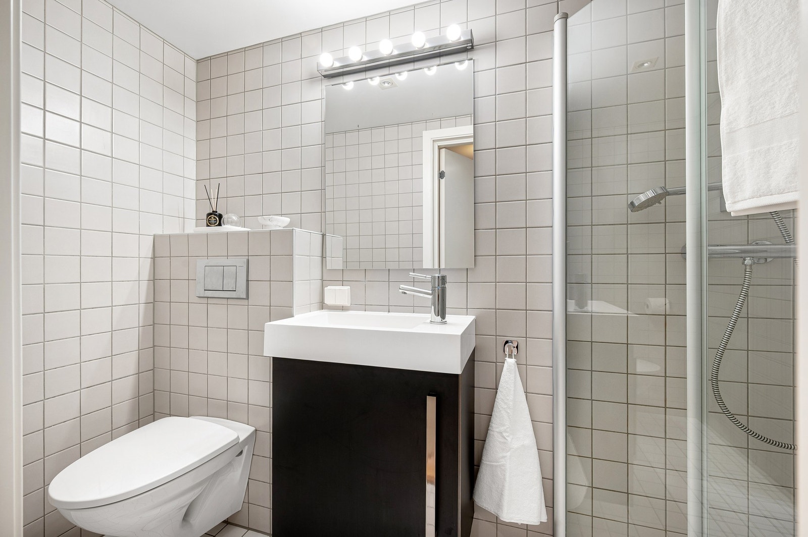 Her får du veggmontert toalett og servant, og åpen dusjplass med innfellbare dusjdører. Galleribilde