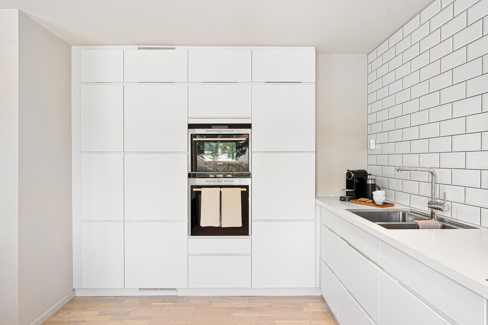 Lyst og pent kjøkken med gjennomført uttrykk, flislagt vegg som gir karakter og godt med skjult oppbevaring Galleribilde