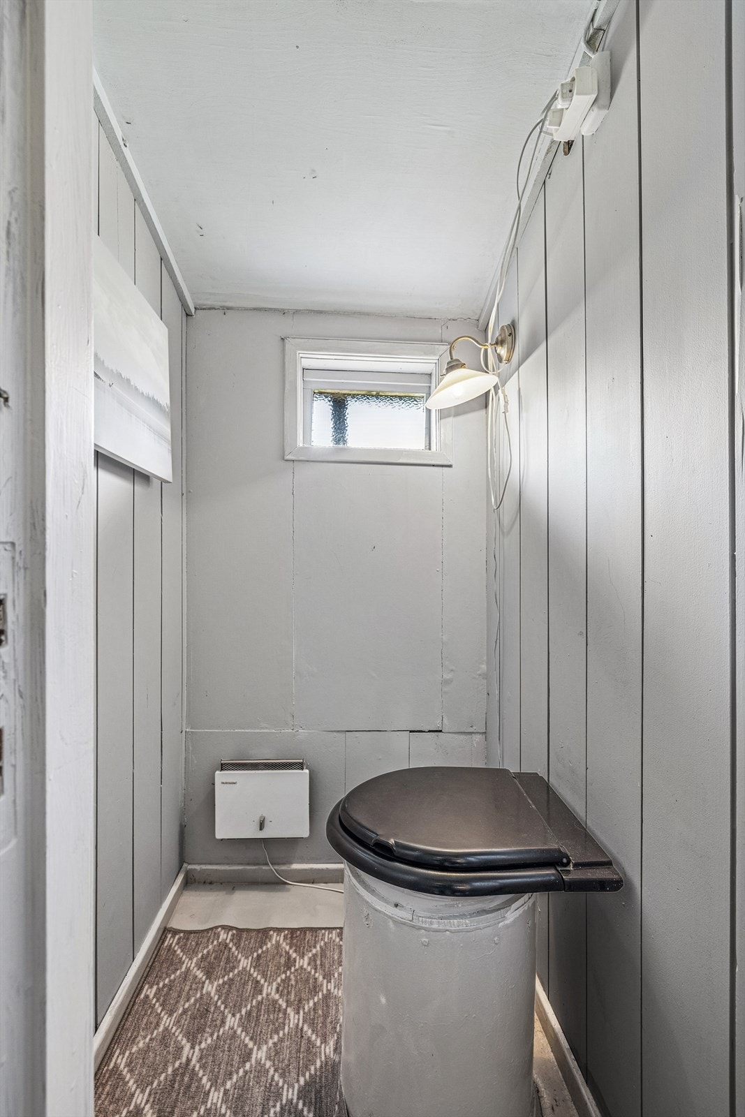 Toalettrom med malt trepanel på gulv, vegger og tak. Rommet er utstyrt med toalett som har åpning rett ned i en enkel utedo/septisk løsning. Galleribilde