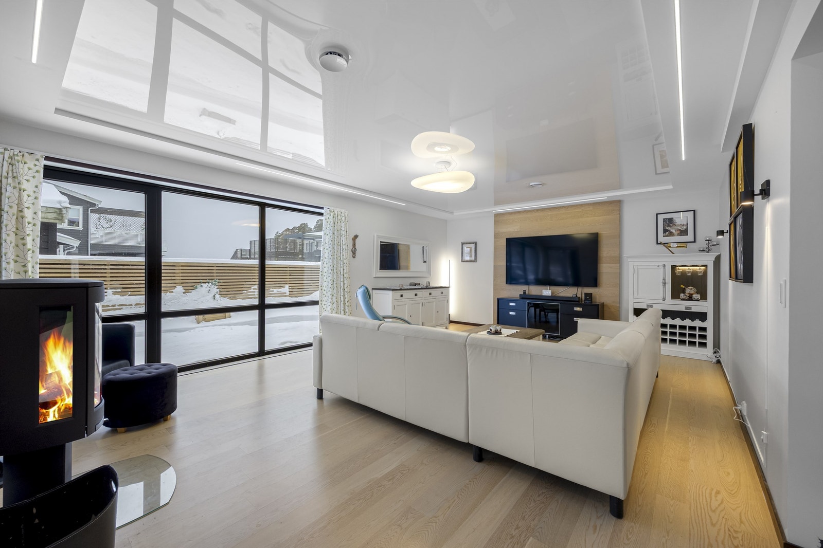 Store vinduer og en moderne peisovn utgjør rommets midtpunkt. Galleribilde