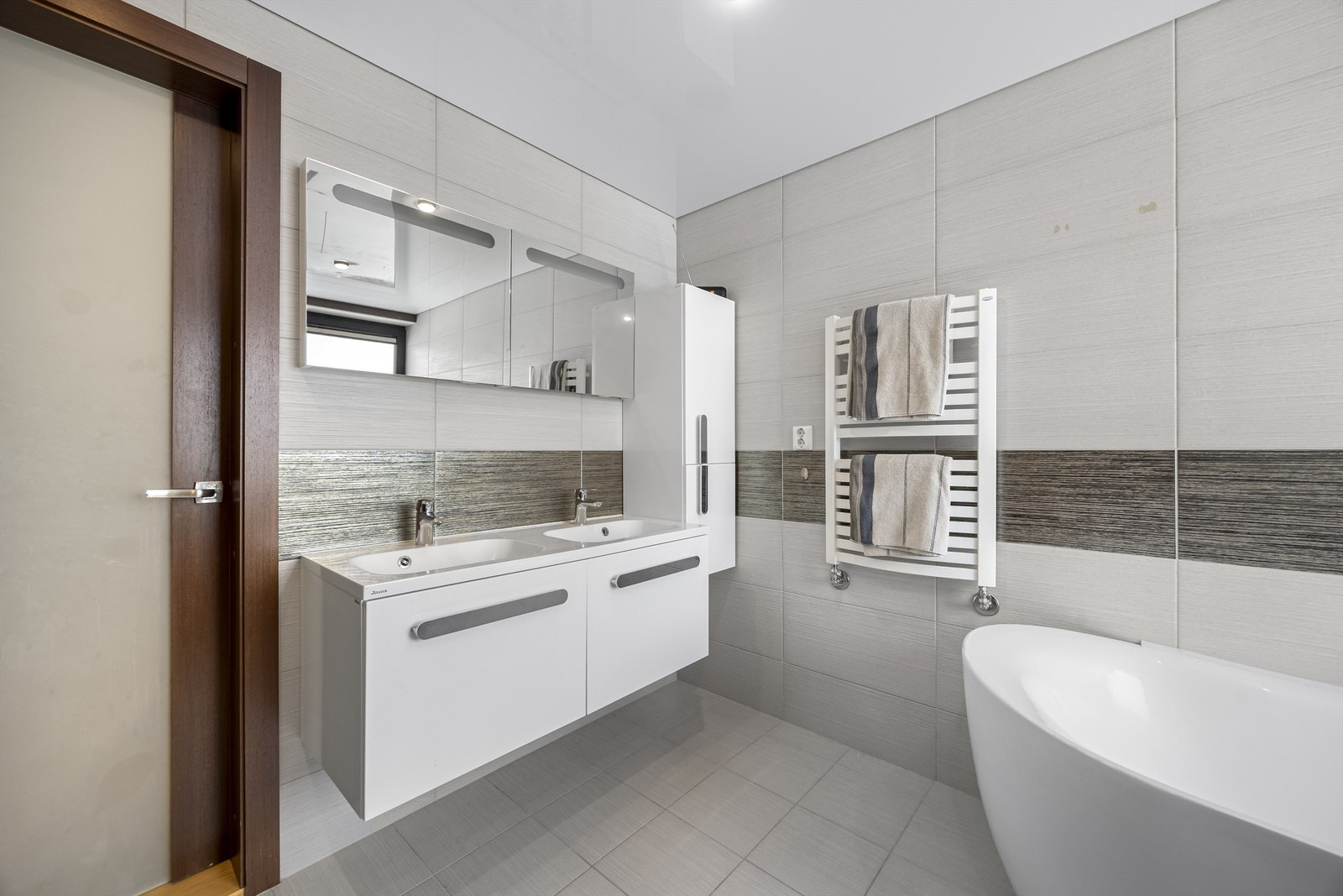 Hovedbadet er delikat flislagt og utstyrt med dobbel servant og håndkletørker. Galleribilde