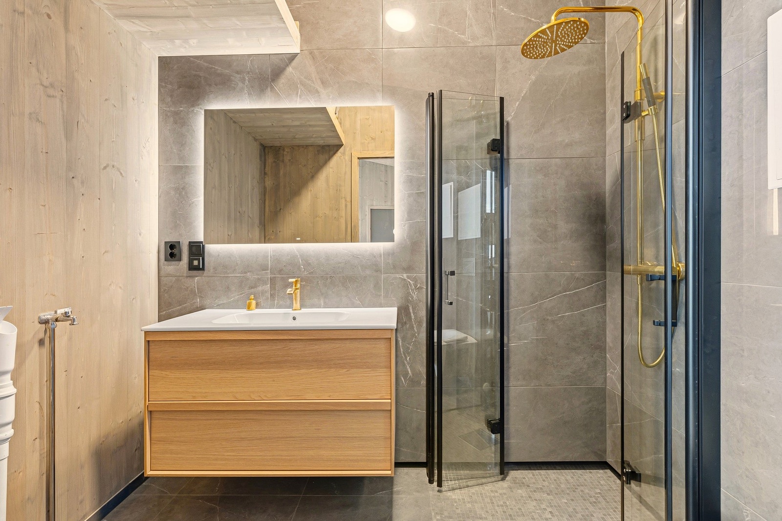 Baderommet er godt utnyttet for å få plass til det mest nødvendige men også lagringsplass. Rommet har kombinert fliser og massivtre på veggene og flislagt gulv med varme. Galleribilde