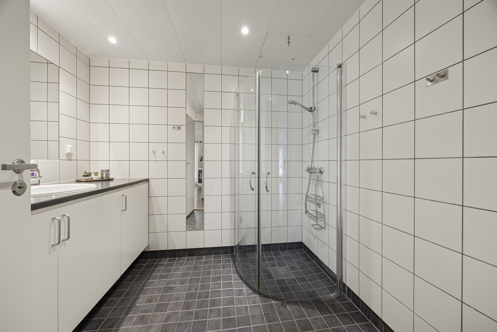 Badet er flislagt og består av speil, servant med seksjon, dusjhjørne og veggmontert toalett. Galleribilde