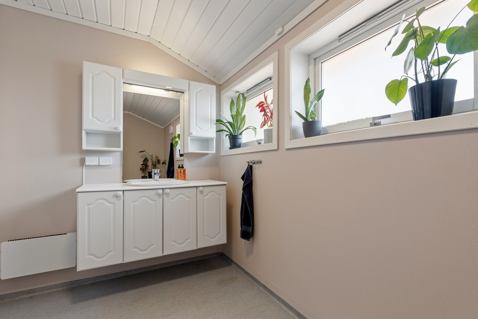 Baderom med profilerte, lyse fronter, overhengende speil, belysning samt sideskap. Galleribilde