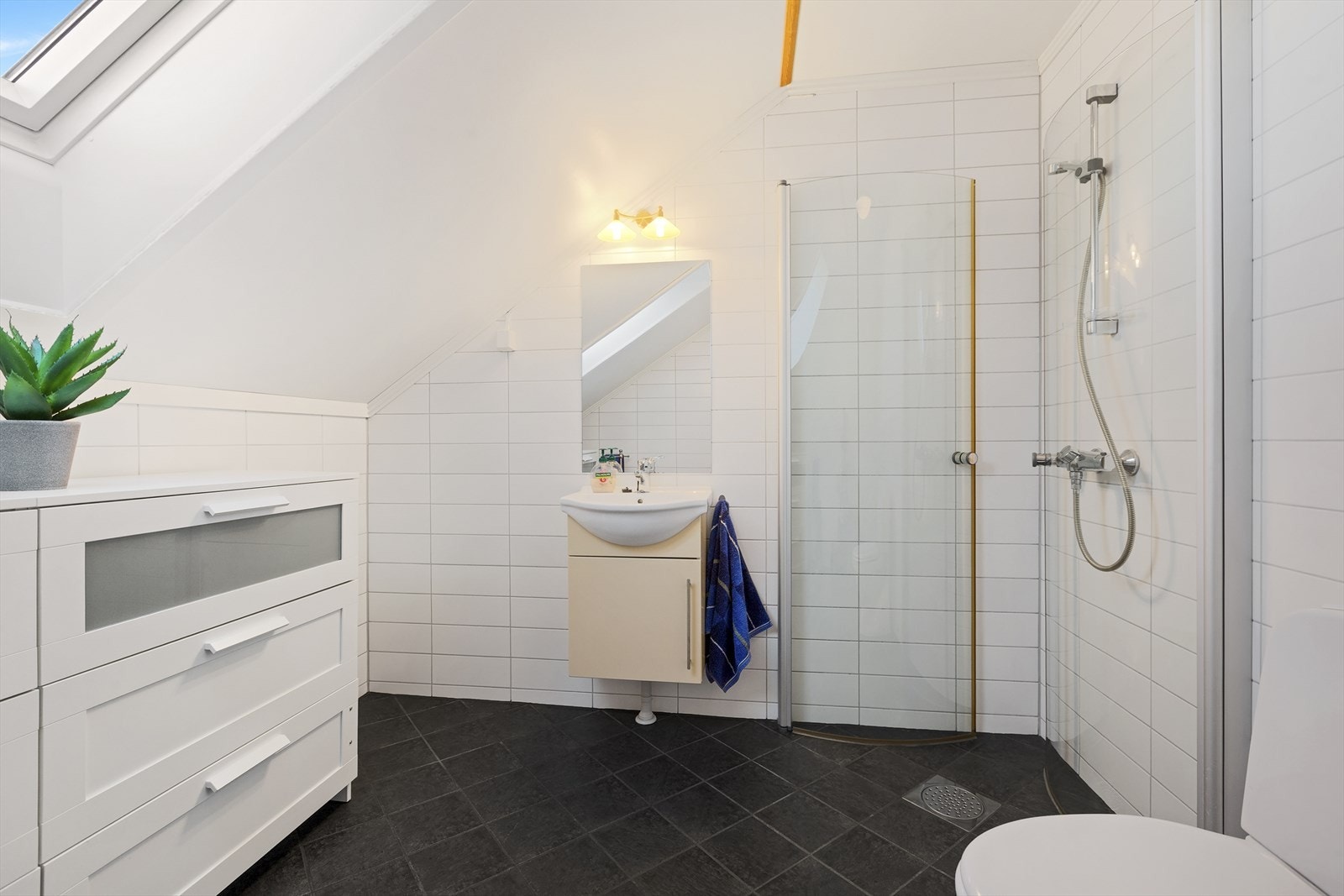 Badet er utstyrt med toalett, servant og et dusjhjørne med svingbare glassdører. Galleribilde