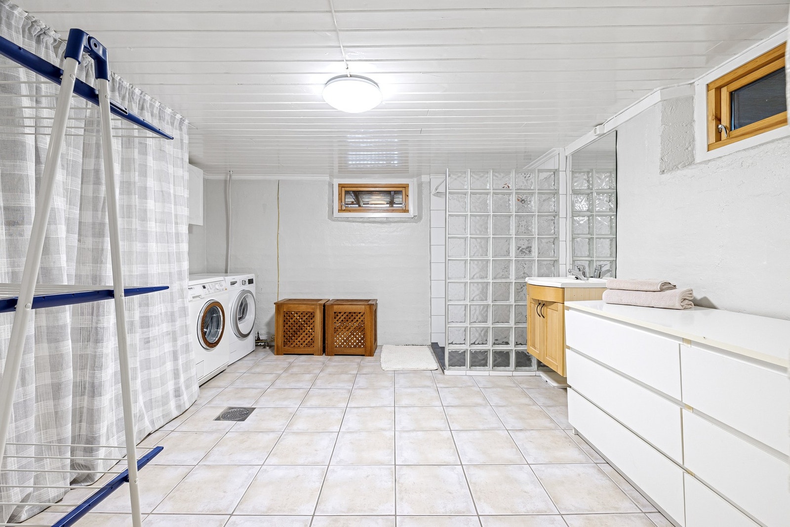 Vaskerommet er innredet med dusjhjørne med glassbyggerstein og dusjforheng. Det er opplegg for vaskemaskin, og varmtvannsbereder og metallvask er plassert bak forhenget. Galleribilde